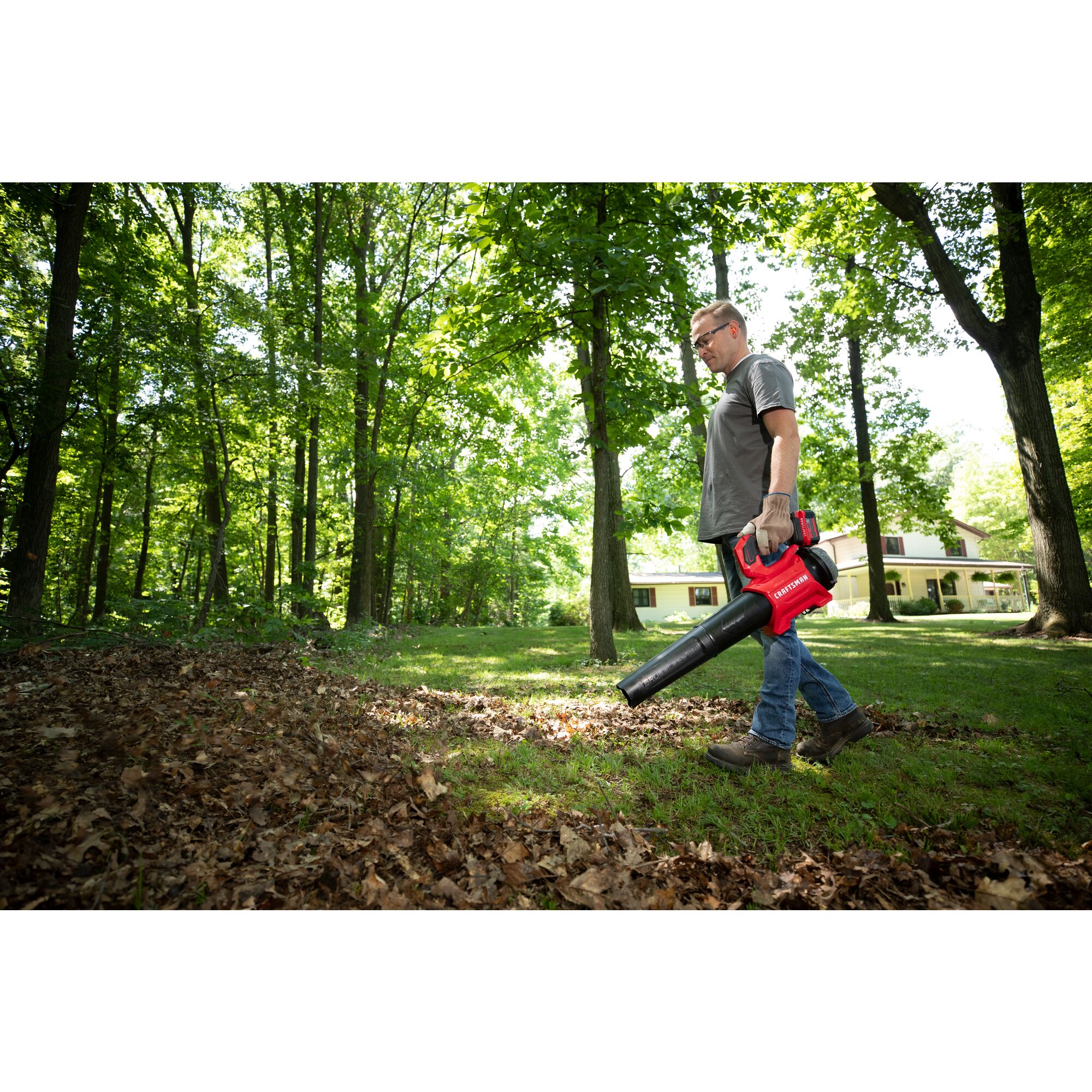 CRAFTSMAN V20 BRUSHLESSRP Blower clearing leaves off grass in a wooded area with tree coverage