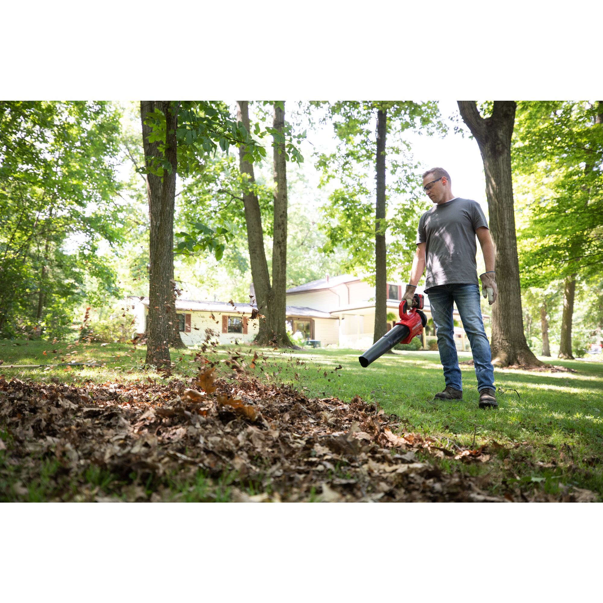 CRAFTSMAN V20 BRUSHLESSRP Blower clearing leaves off grass in a wooded area with tree coverage